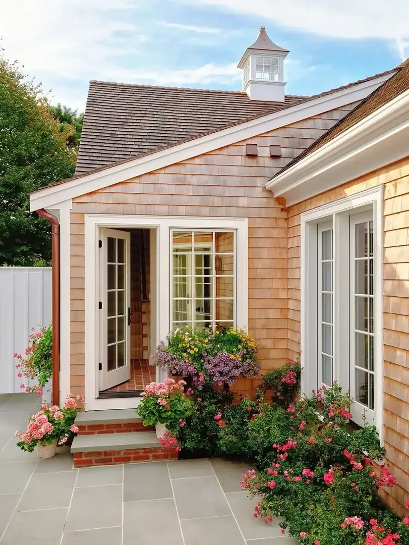 Cedar shingle cottage with white cupola and rose garden beds