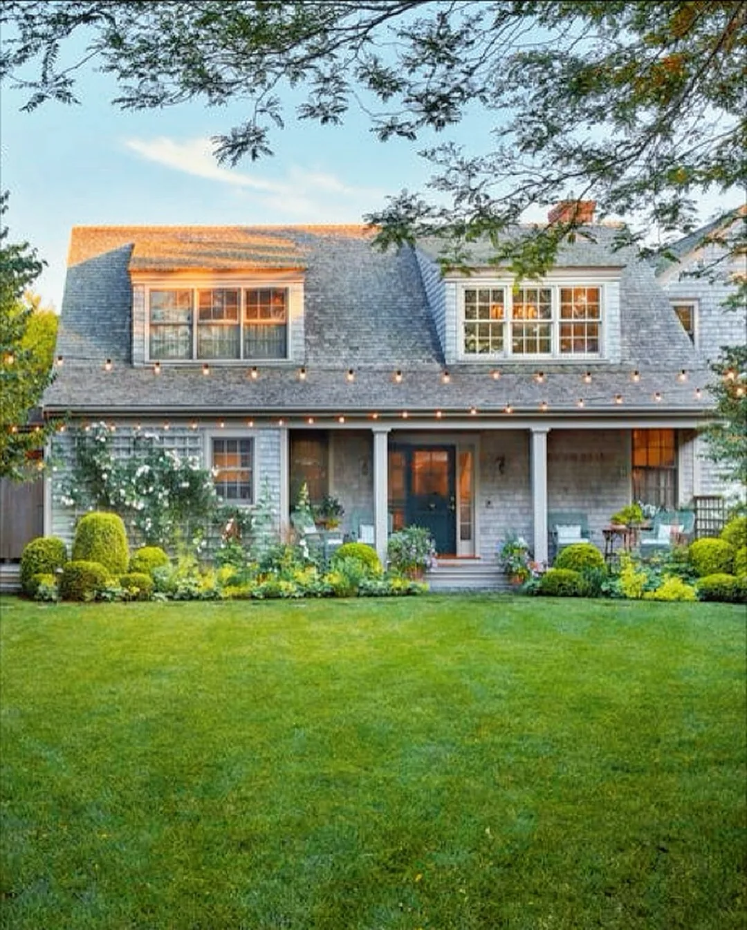Shingled cottage with string lights over a green lawn