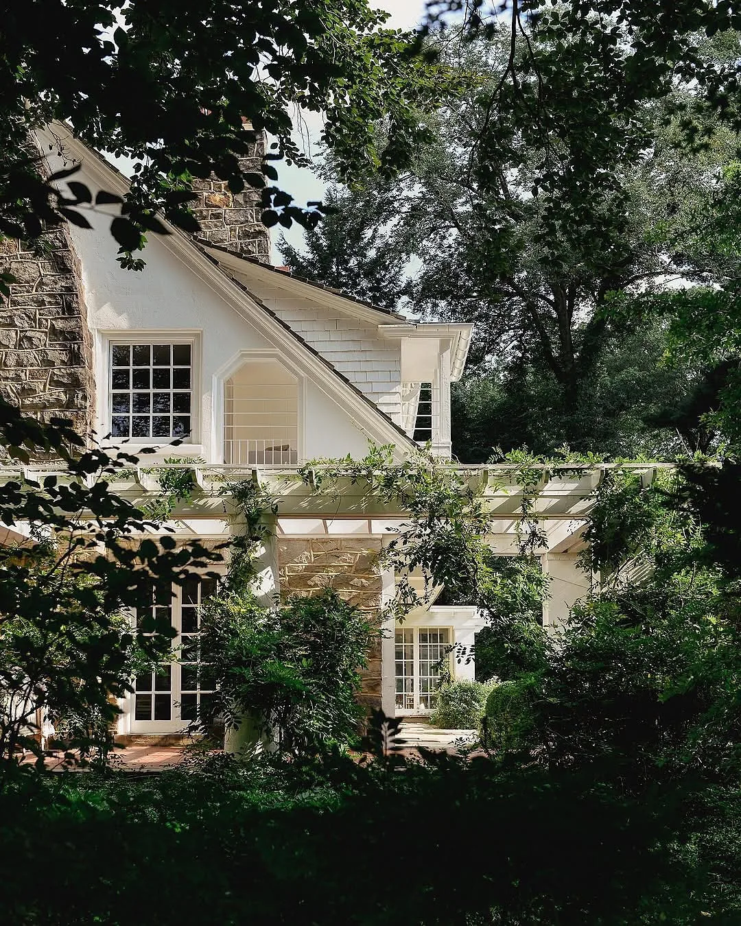 Stone and shingle house with a pergola covered in climbing vines