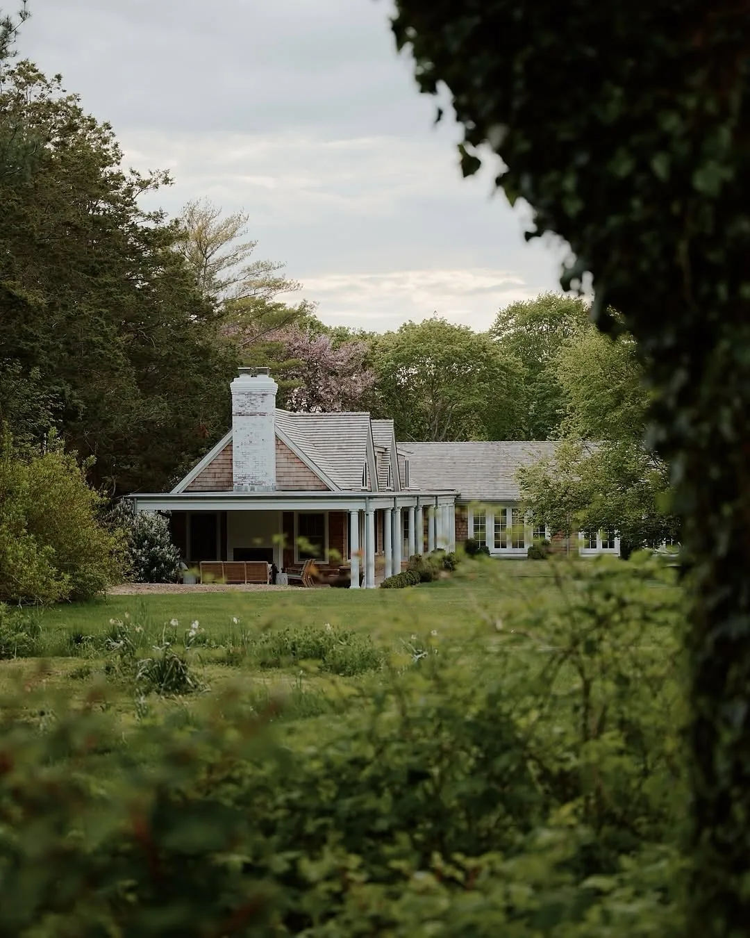 White shingle cottage with a chimney in a meadow garden