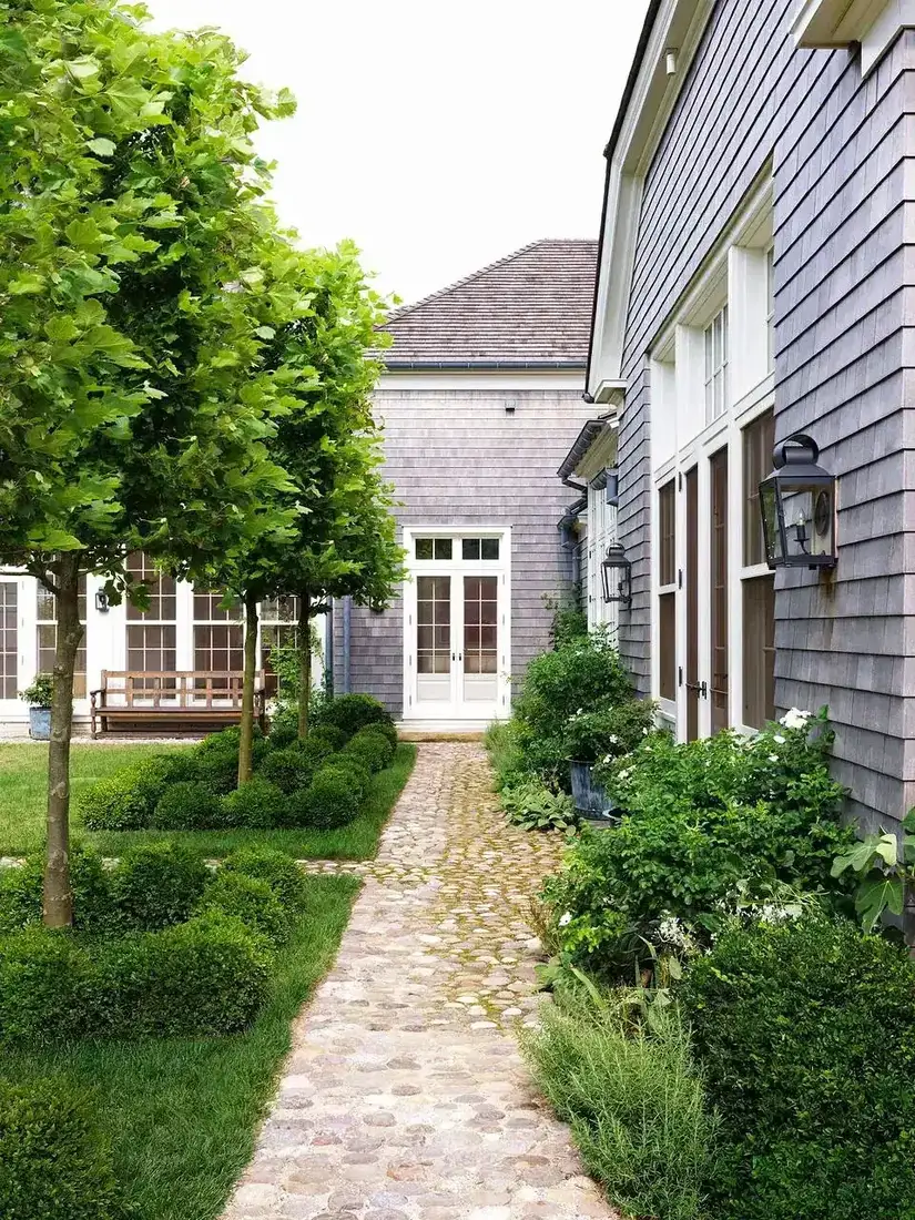 Grey shingle house with cobblestone garden path and hydrangeas