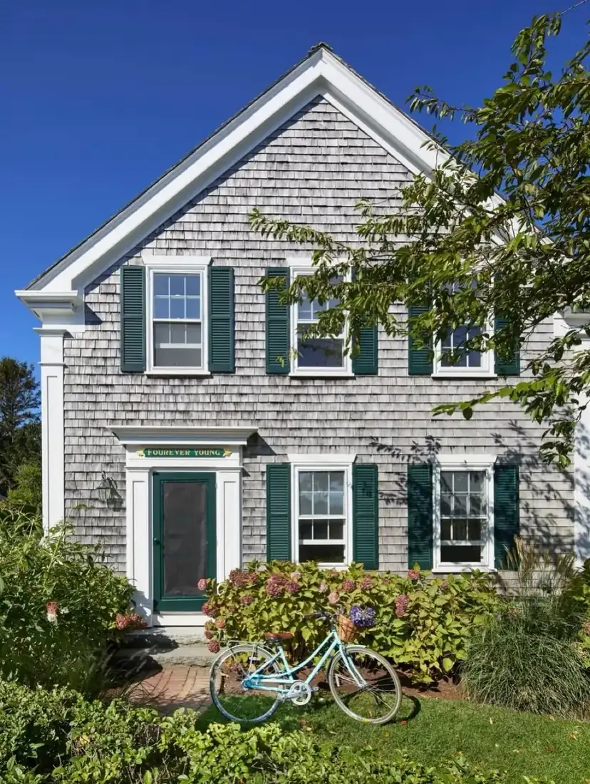 Grey shingle saltbox house with green shutters and bicycle by the front steps