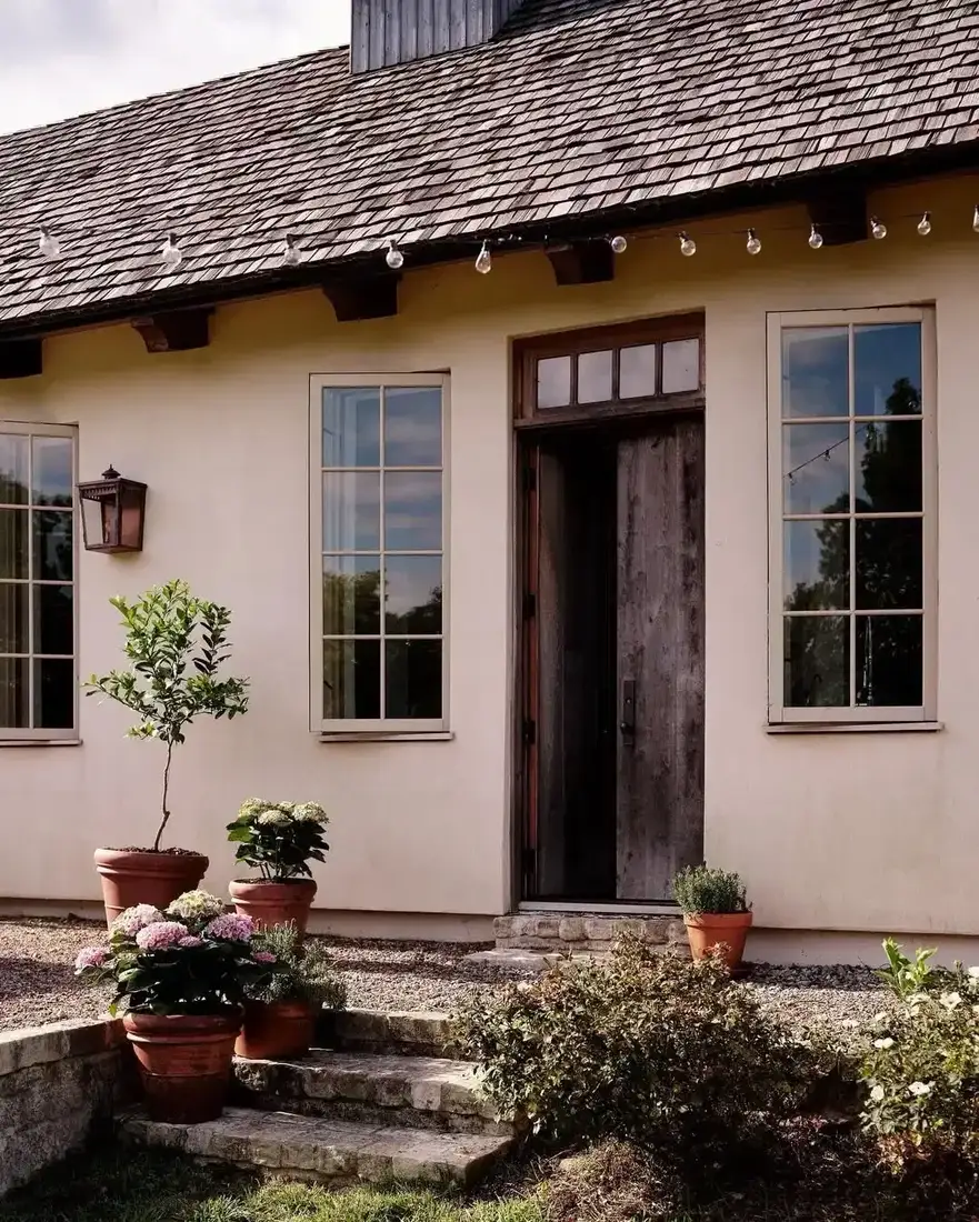 Pink stucco cottage with cedar shingle roof and clay pots in courtyard