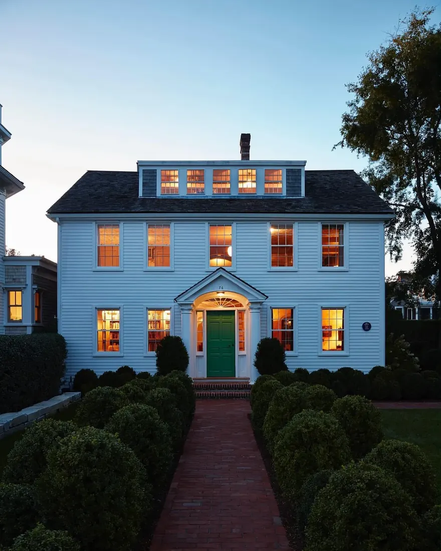 Pale blue colonial house with green front door and low boxwood hedges
