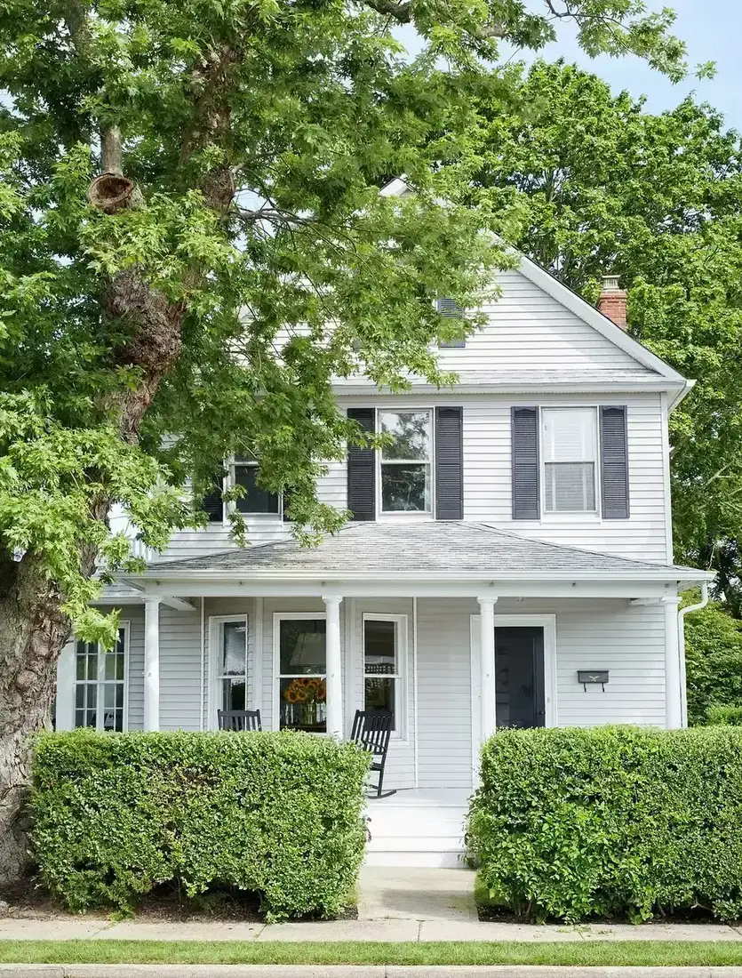 White clapboard colonial with black shutters and clipped boxwood hedges