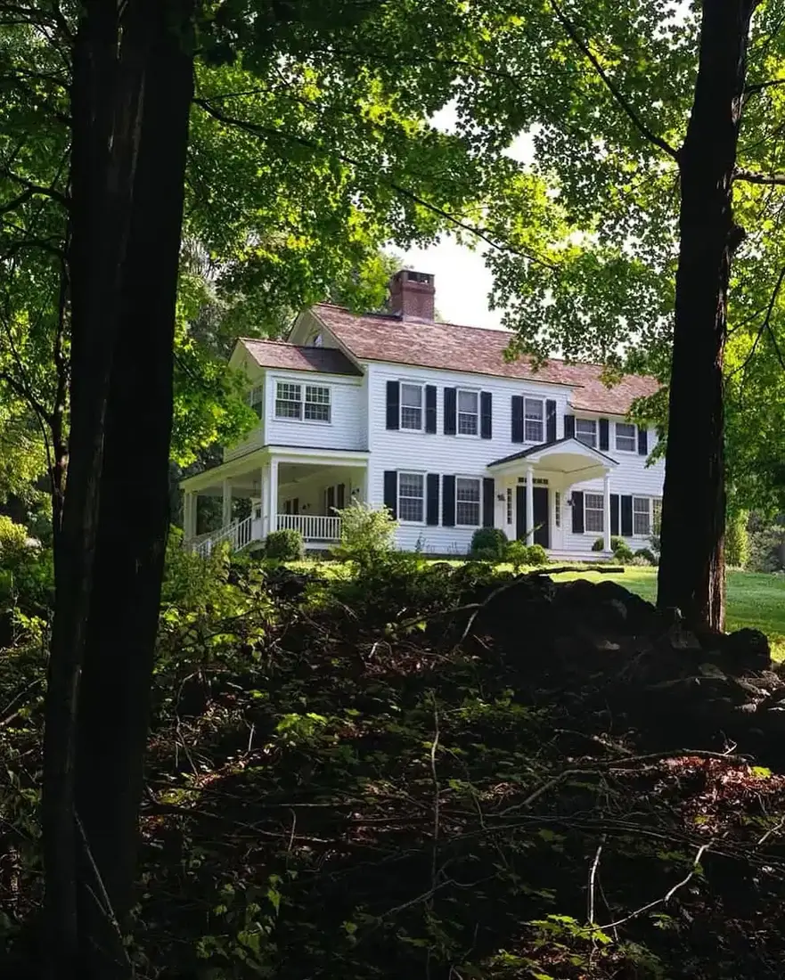 White colonial house with black shutters set among woodland trees