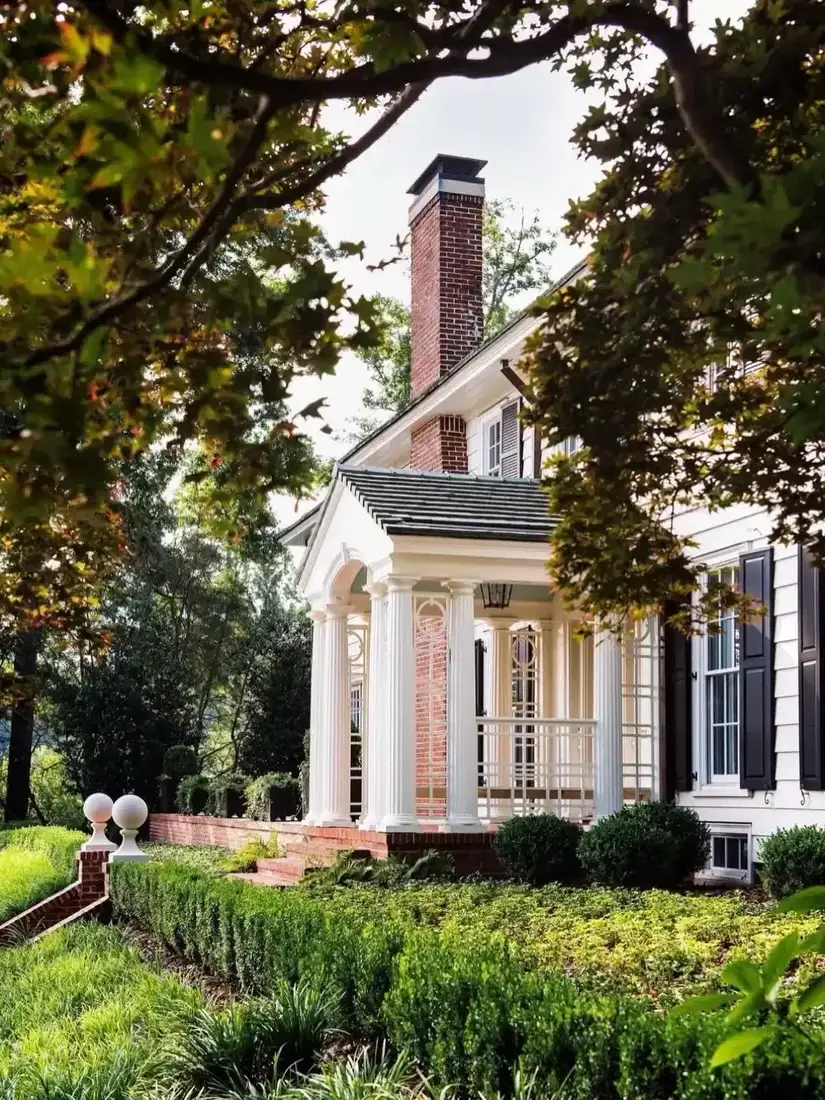 White colonial with columned portico and clipped boxwood shrubs