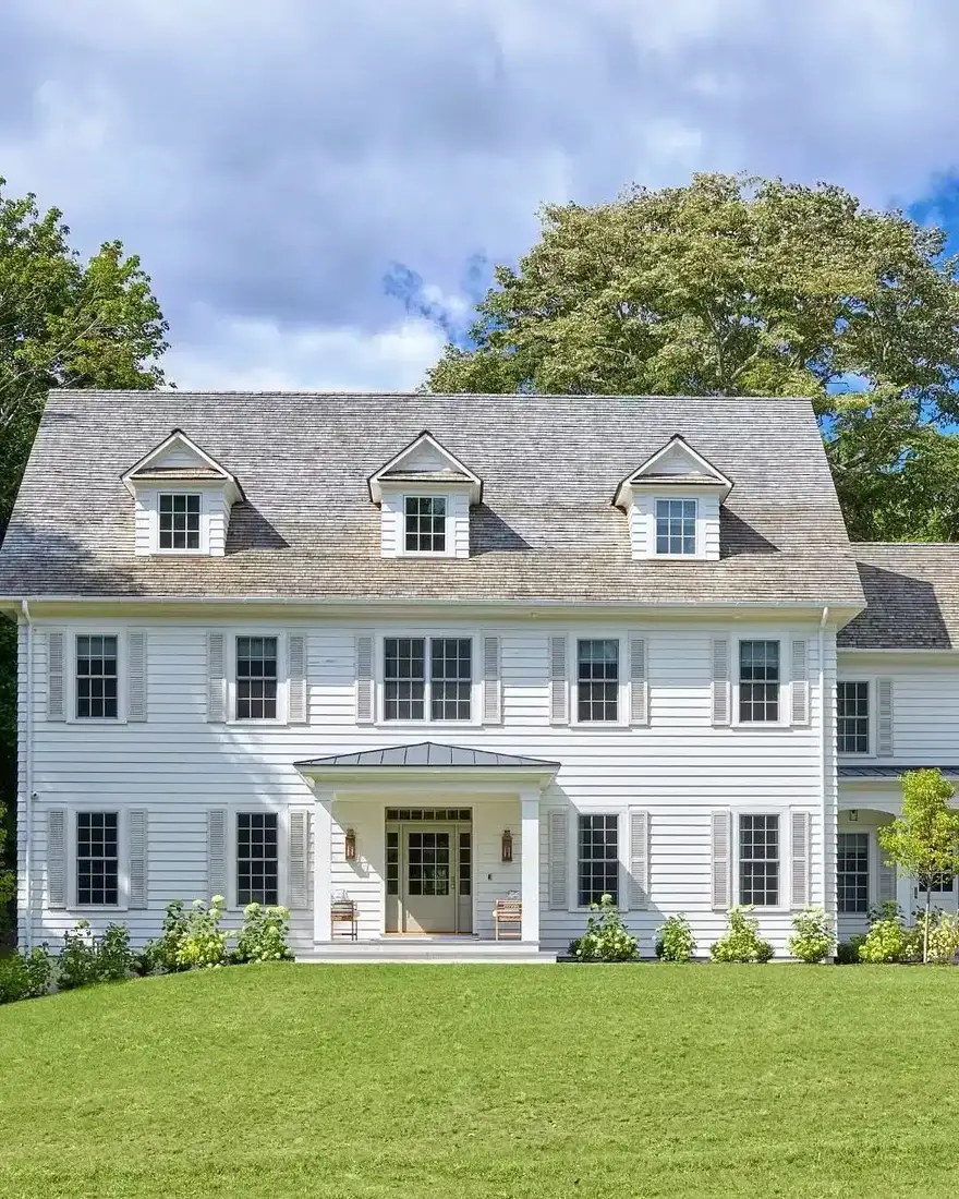 White colonial house with black shutters and three dormer windows on the roof