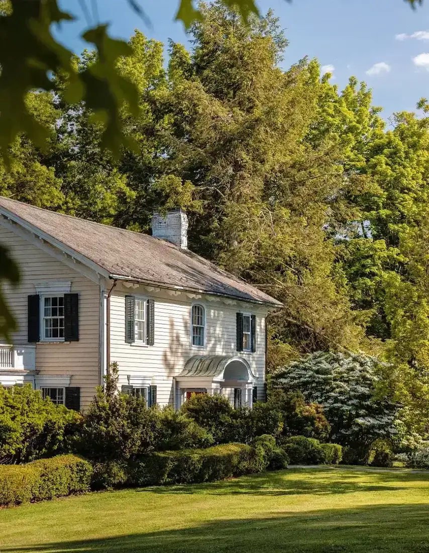 White colonial house with black shutters set on a wide green lawn