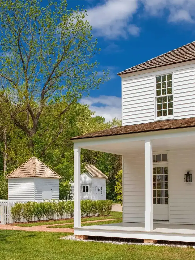 White colonial house with porch, picket fence and outbuildings