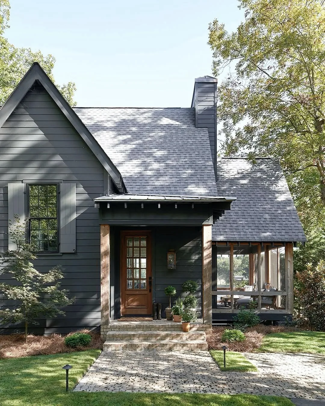 Dark gray cottage with a wood door and gravel path