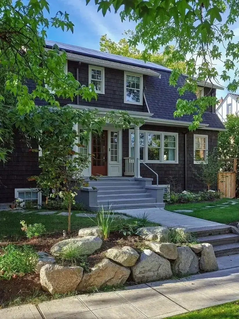 Dark shingle house with large boulders and planted landscaping