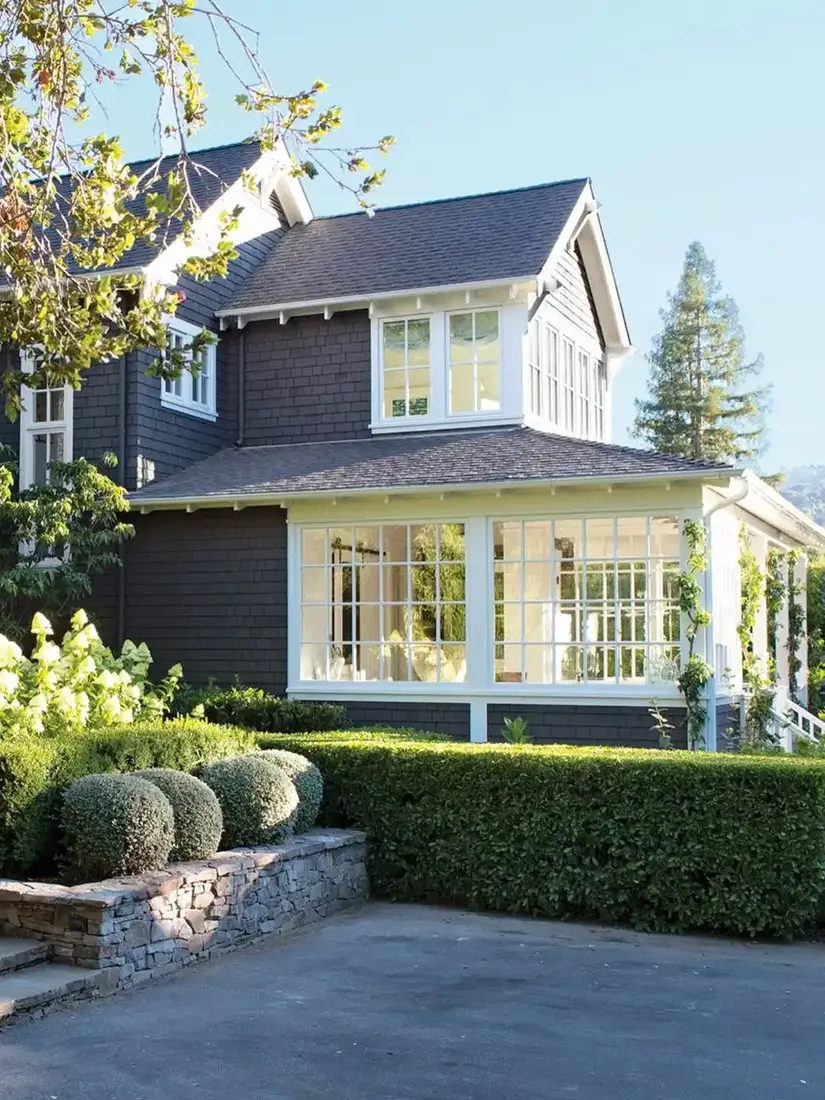 Dark shingle house with white framed sunroom and clipped hedges