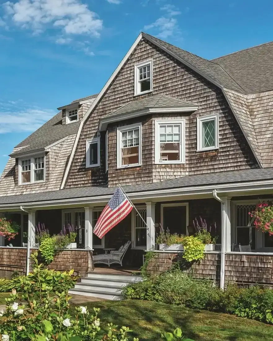 Grey shingle gambrel house with American flag by the front porch