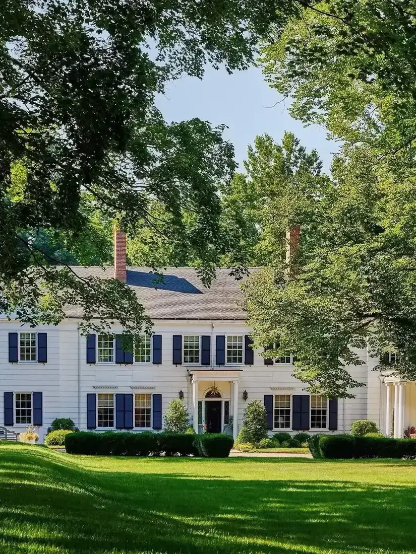 Long white farmhouse with soft blue shutters facing a wide flat lawn