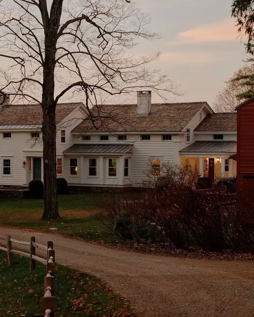 White clapboard farmhouse with red barn further down a gravel lane