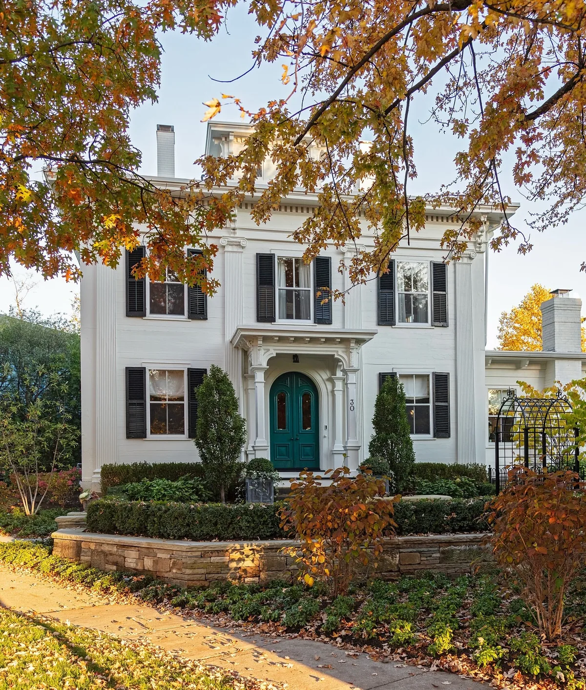 White Greek Revival house with a teal door in autumn