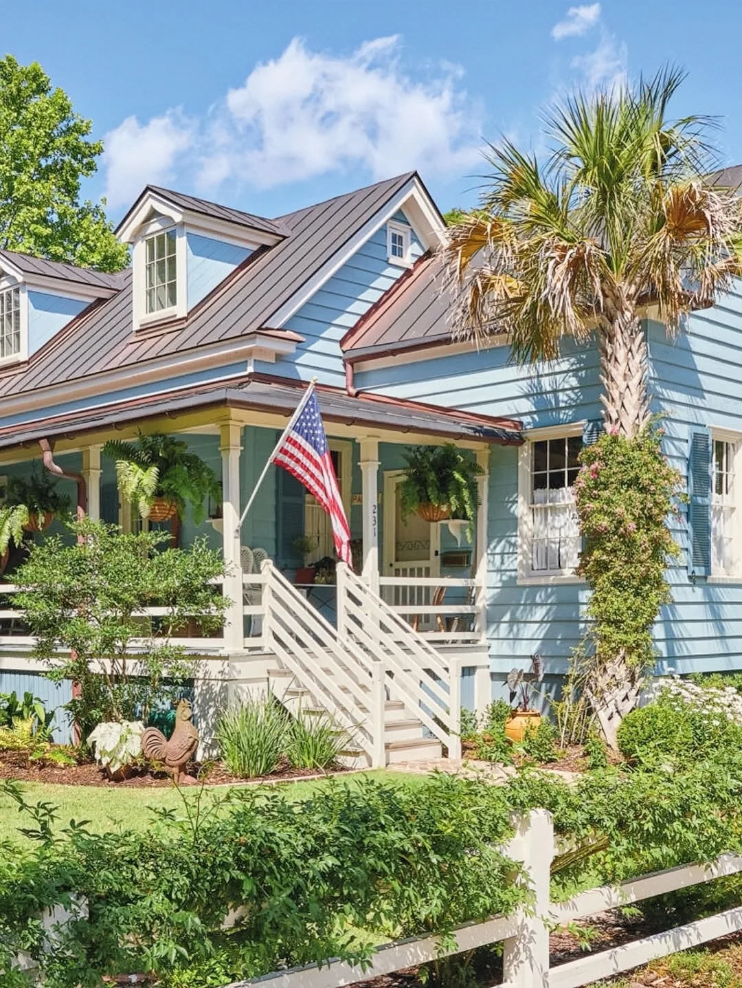 Blue lowcountry cottage with a dark metal roof and palm trees in front