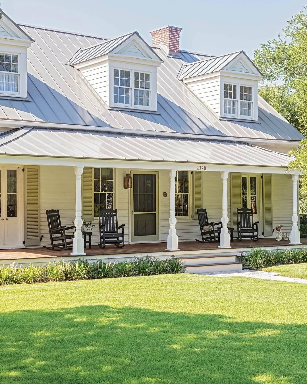 Cream cottage with a metal roof, dormers and rocking chairs on the porch