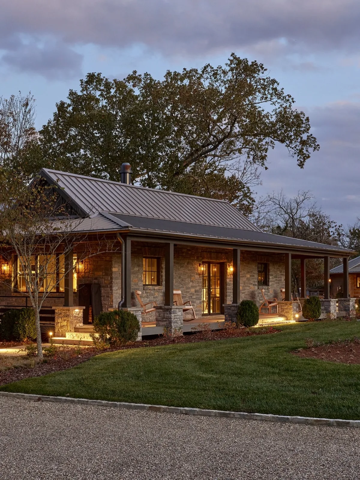 Stone ranch house with a metal roof and a lit porch at dusk