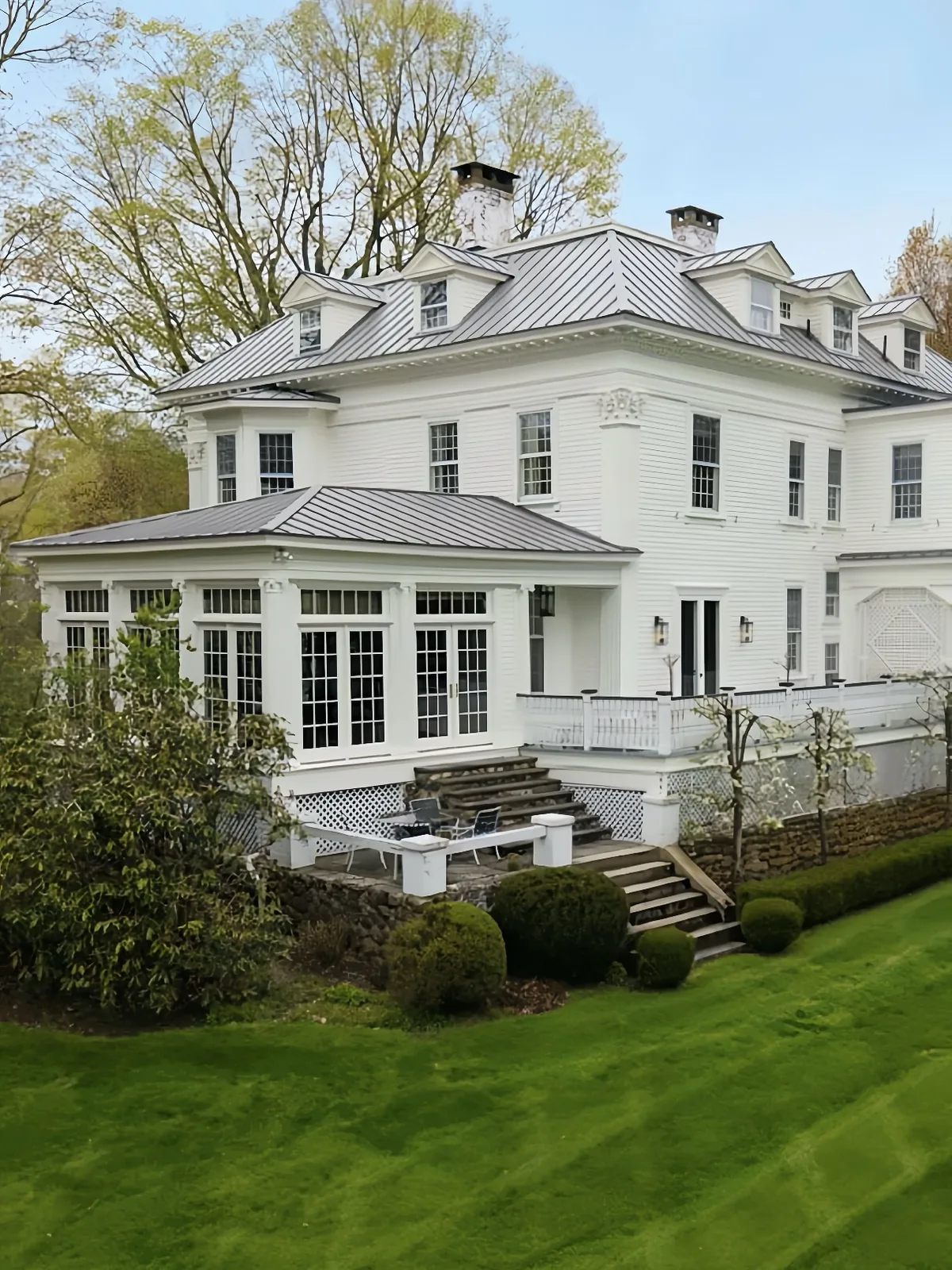White clapboard farmhouse with a metal roof behind a wide lawn