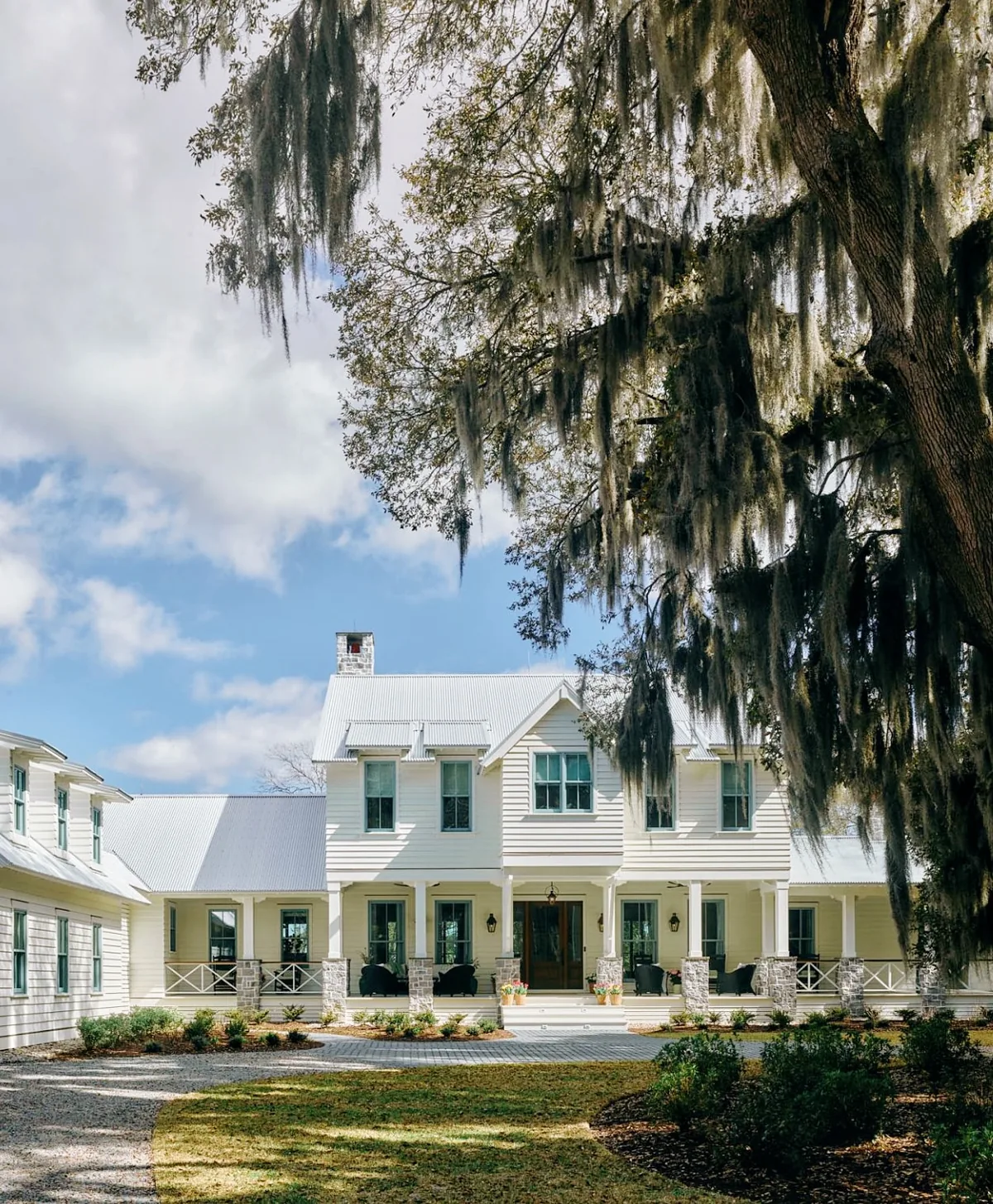 White plantation style house with a metal roof under live oaks