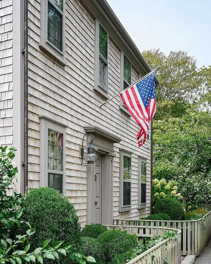 Cedar shingle colonial house with American flag and clipped boxwood hedge along the front