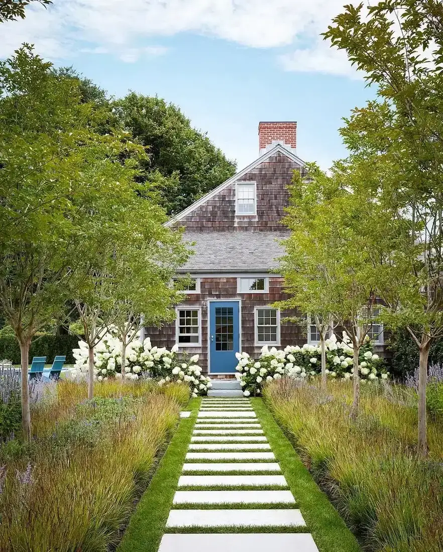 Shingle cottage with blue front door and hydrangea lined walkway