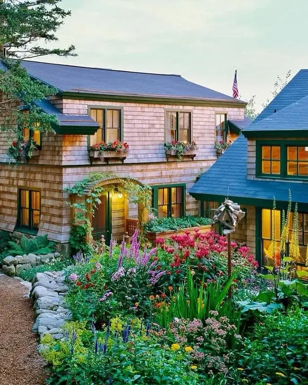 Shingle cottage surrounded by cottage garden flowers and green lawn