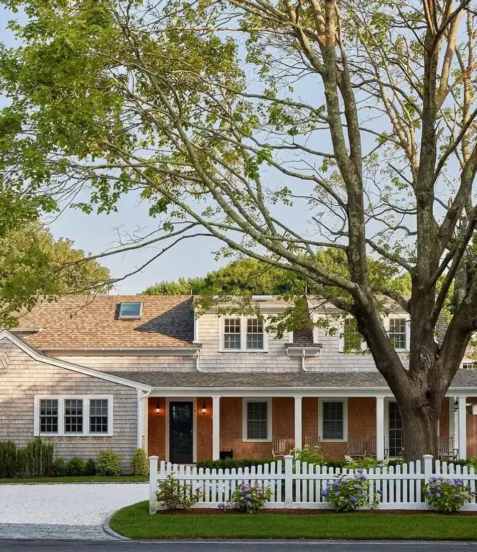 Shingle cottage with white picket fence and hydrangeas along the front