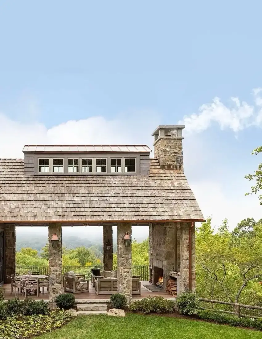 Shingle lodge with stone columns and outdoor fireplace on the porch