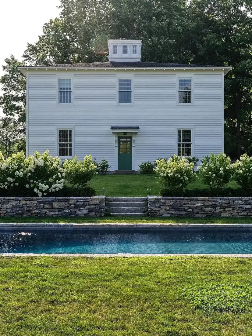 White clapboard house with cupola and pool stone terrace in the garden