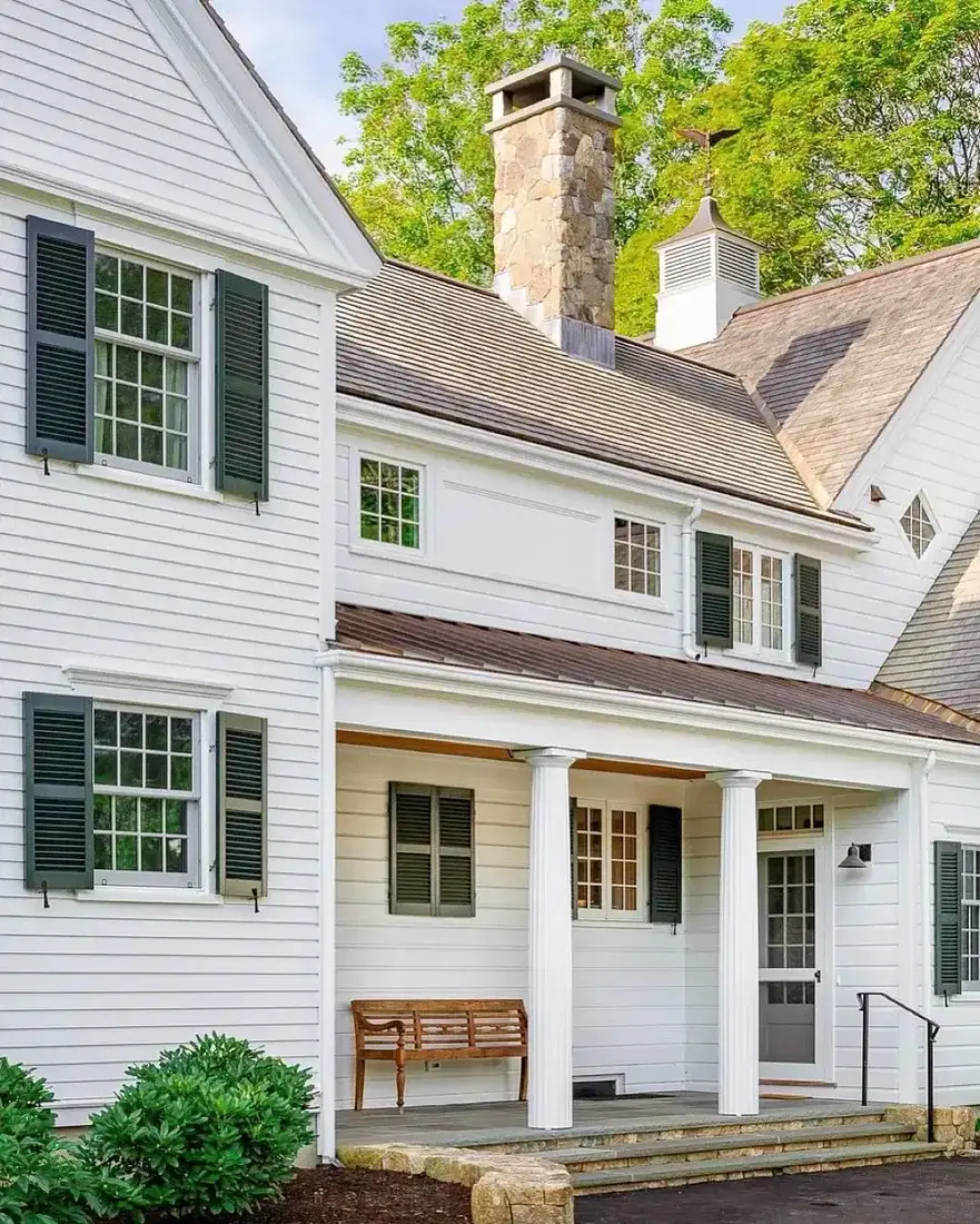 White clapboard house with tall fieldstone chimney and cupola on the roof