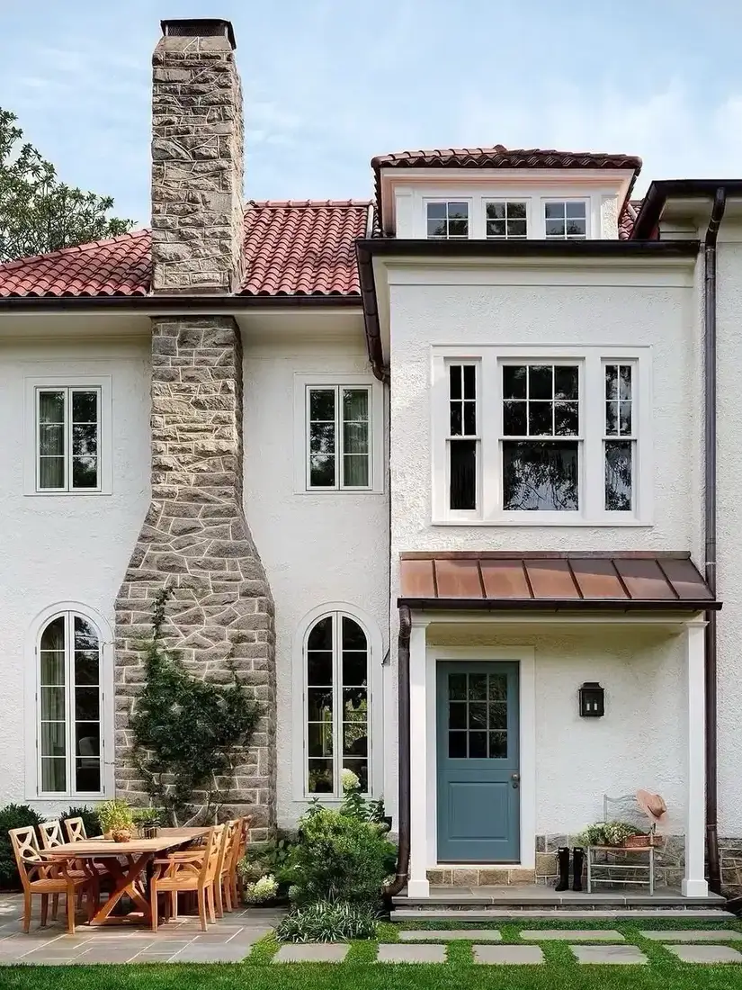 White stucco house with stone chimney and warm clay tile roof