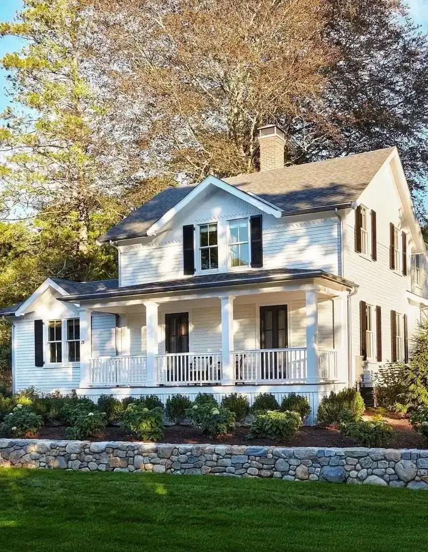 Pale blue cottage with white porch and low stone wall along the front