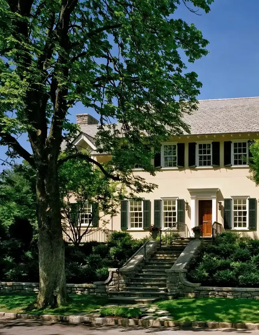 Pale yellow colonial house with green shutters and stone front steps