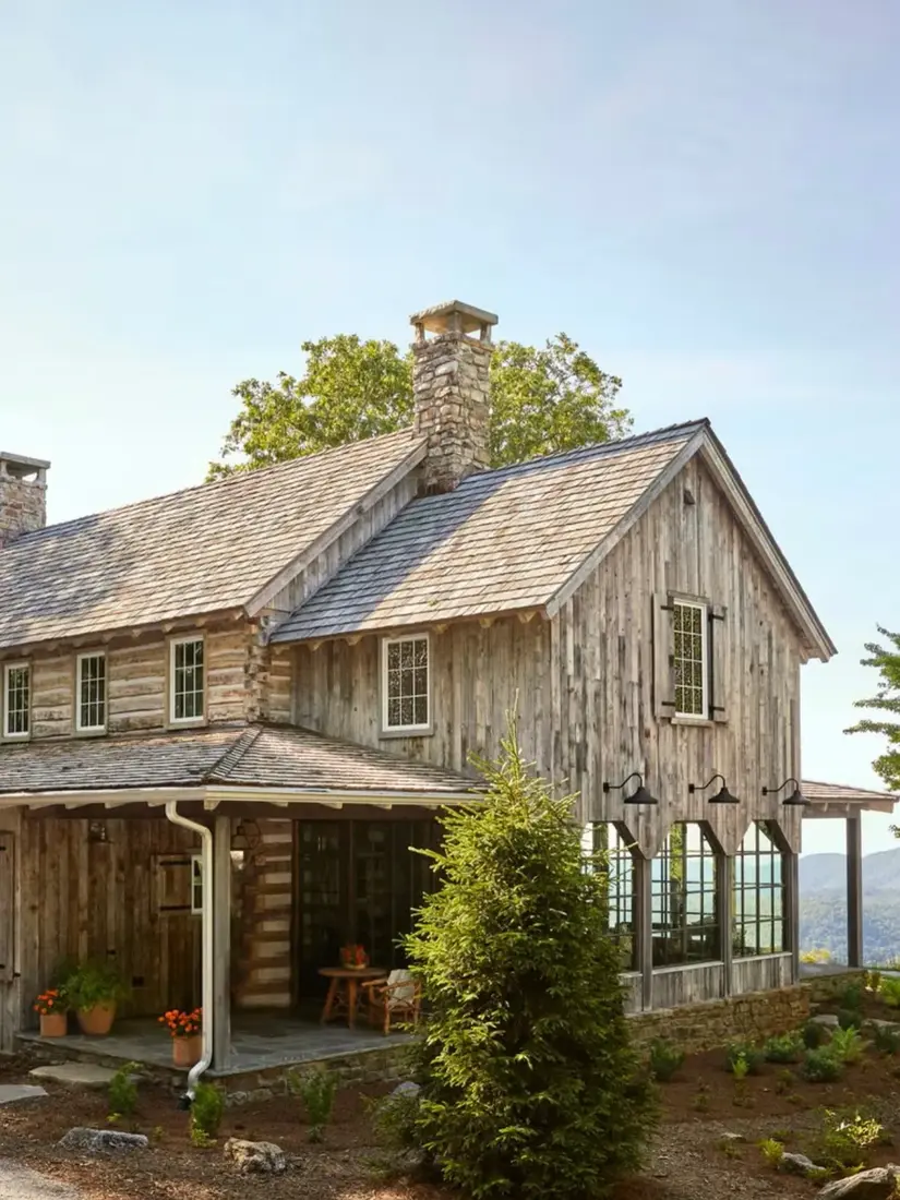 Reclaimed barnwood house with tall fieldstone chimney and dark windows
