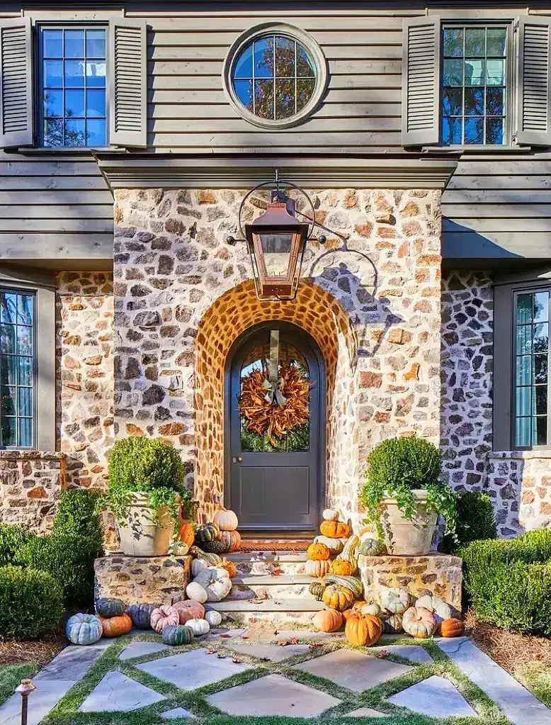 Rustic stone front porch decorated for fall with pumpkins and mums