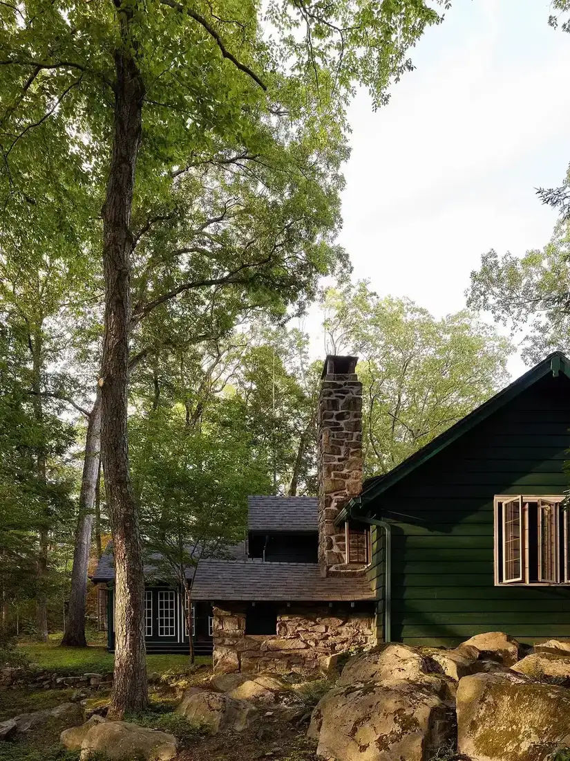 Green cabin with large stone chimney set among boulders and pine trees
