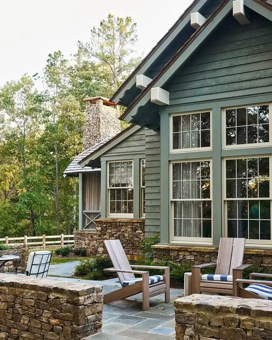 Green craftsman cottage with stone patio and dark green Adirondack chairs