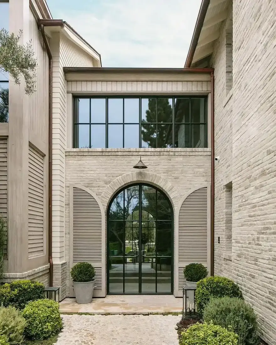 Limestone courtyard with tall arched steel doors and pale gravel