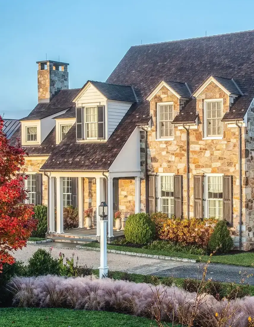 Mixed stone house with white dormers and tall ornamental grasses in front