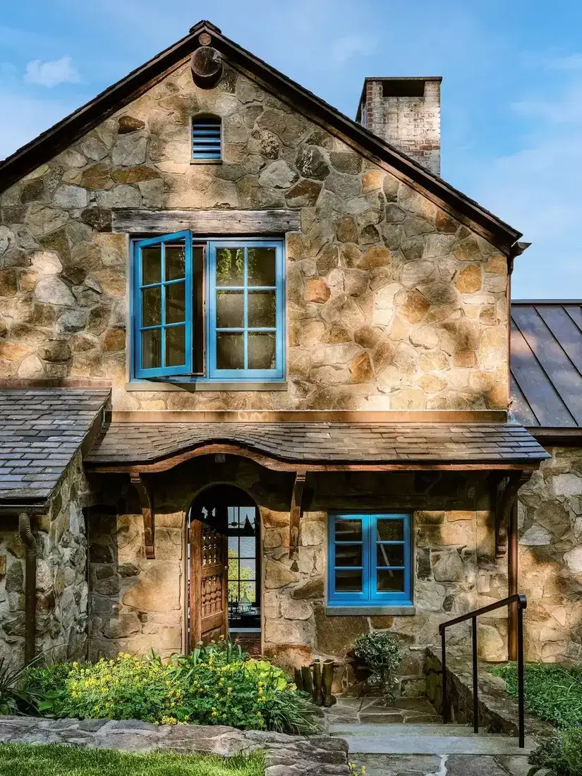 Stone cottage with turquoise shutters and arched front door with stone surround