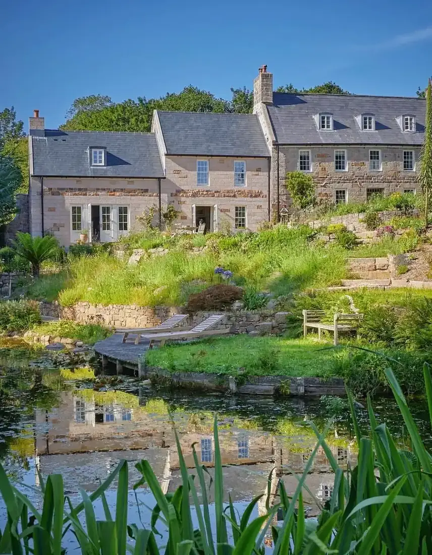 Stone farmhouse with slate roof and small pond garden with grasses
