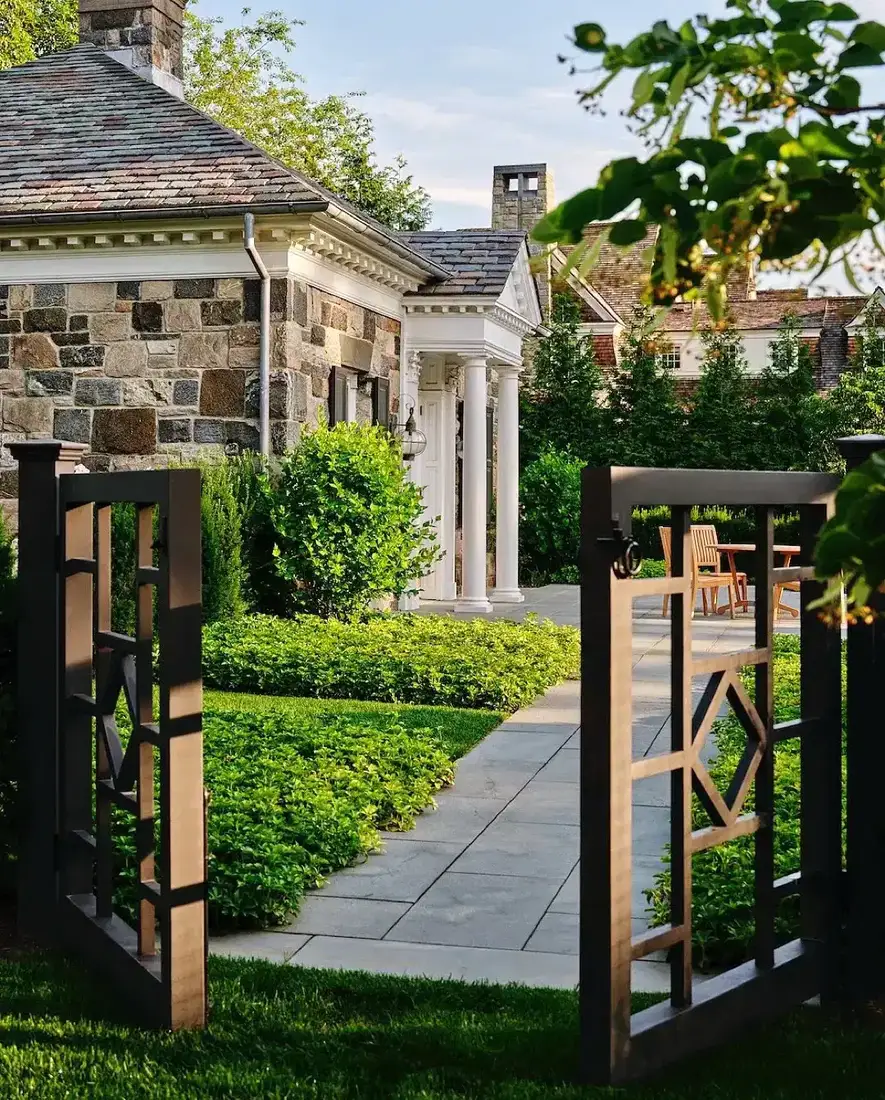 Stone house with boxwood walkway and modern dark metal gate