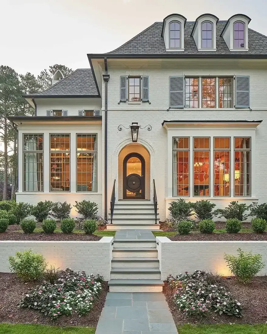 Modern stone farmhouse with large black framed windows and a pale gravel forecourt