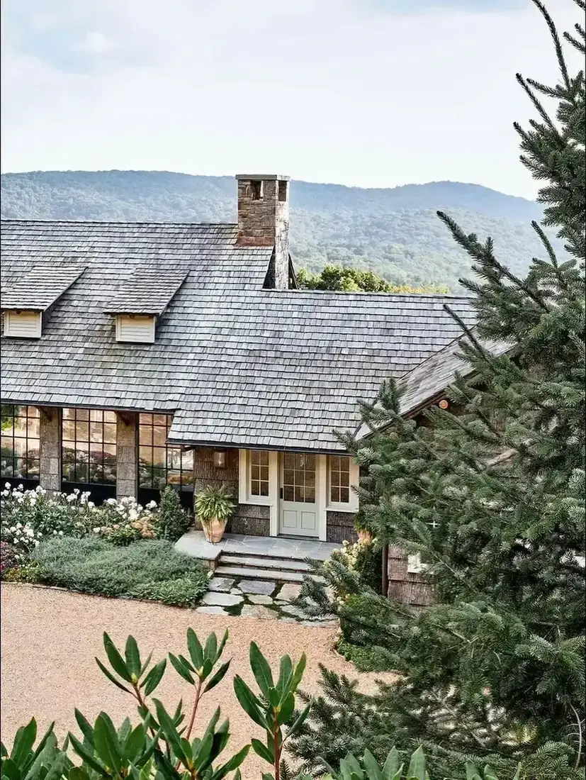 Mixed stone house with white dormer windows and tall ornamental grasses across the front border