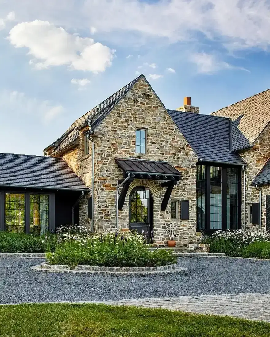 Stone house with slim black steel windows under a warm terracotta tiled roof