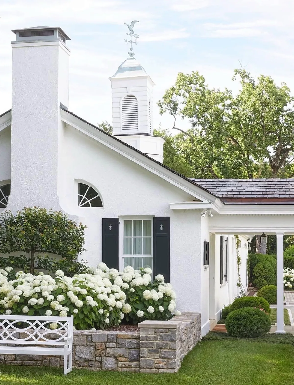 White stucco cottage with black shutters and hydrangeas