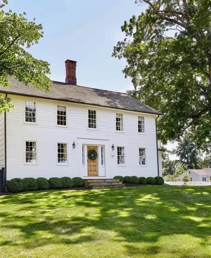 White colonial farmhouse with wreath on the front door and low stone wall